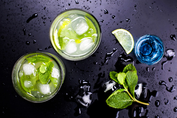 Tasty fragrant refreshing mojito with lime and mint on wet black table in bar or restaurant. Blue liqueur and cocktail mojito.